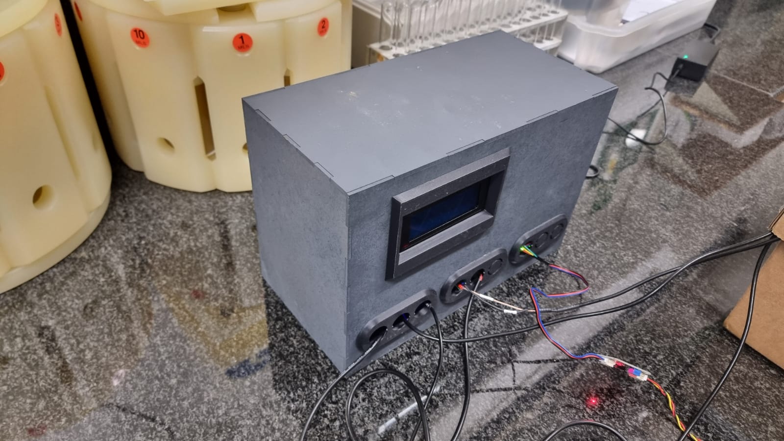 The low-cost monitoring enclosure with LCD and sensor ports beside labelled sample vessels